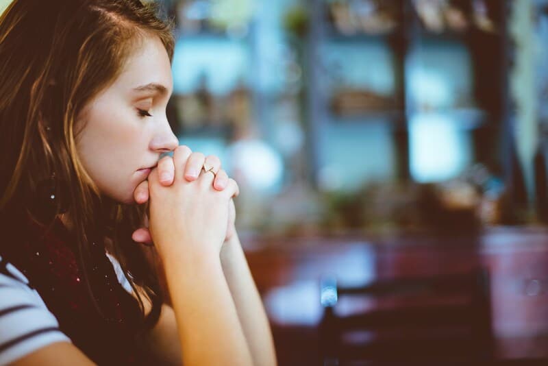 A young woman with closed eyes and hands clasped in prayer, expressing calm and focus, symbolizing the practice of starting each month with gratitude