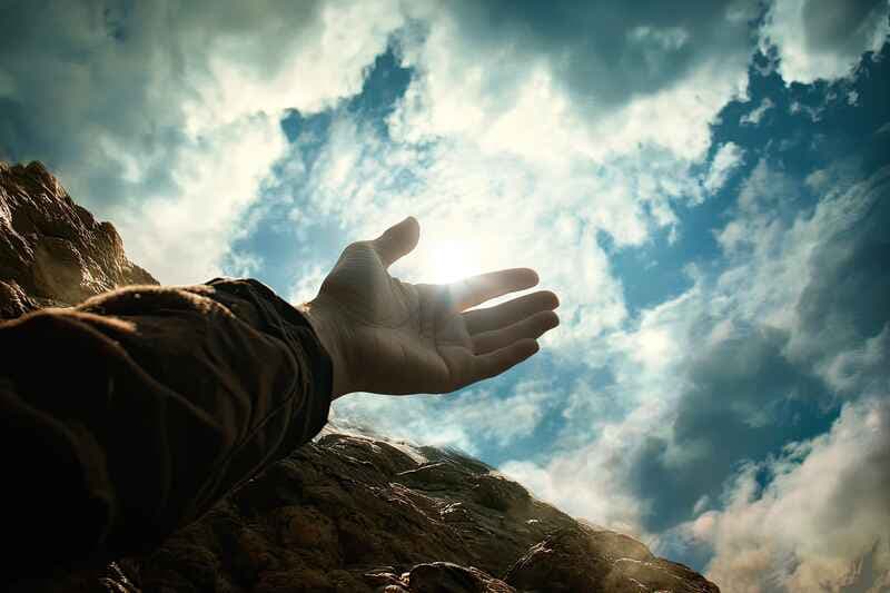 A hand reaching toward the sky with light breaking through clouds, symbolizing the concept of faith