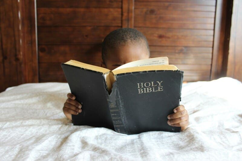 Young child reading the Bible symbolizing early engagement with religious texts and the concept of developing understanding from a young age.